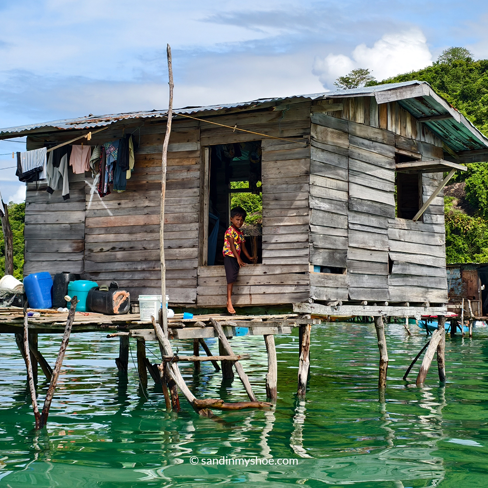 Boy from Sea Gypsy Malaysia village looking through a wooden window