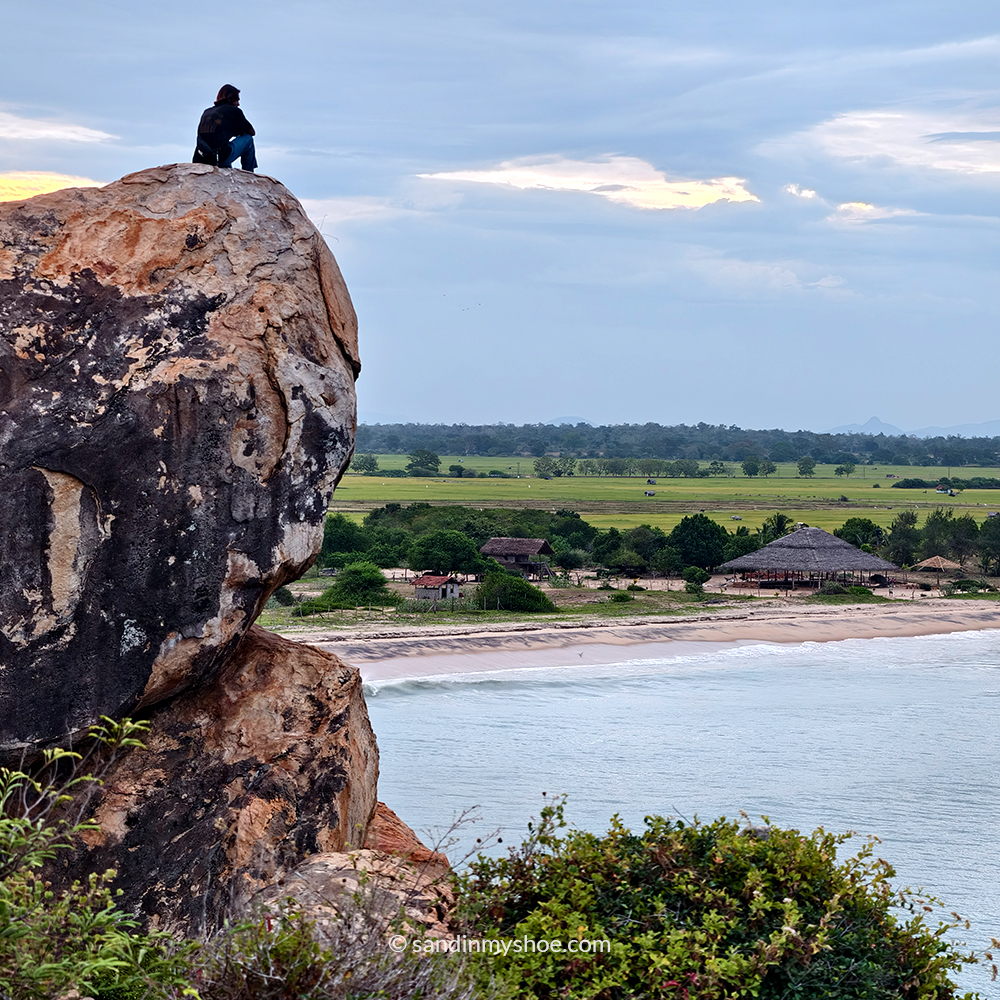 A traveler reflects on a rock above Arugam Bay beach, a peaceful stop on an east coast tuk tuk route in Sri Lanka.