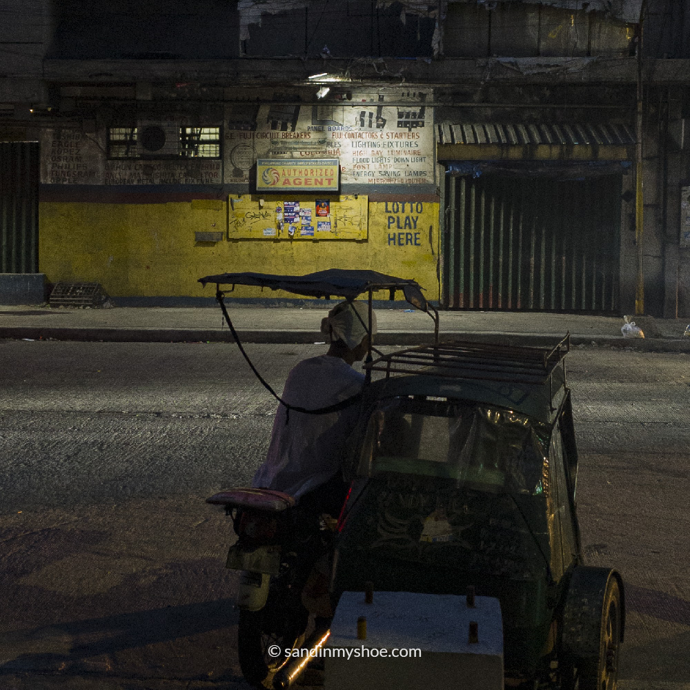 A motorbike taxi driver waits for passengers under a flickering streetlight in Manila