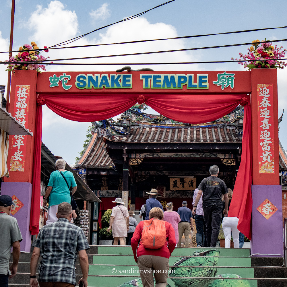 Exterior signage and decorative elements outside the Snake Temple in Penang, indicating the temple’s name and a picture of a snake on the stairs leading to the snake temple..