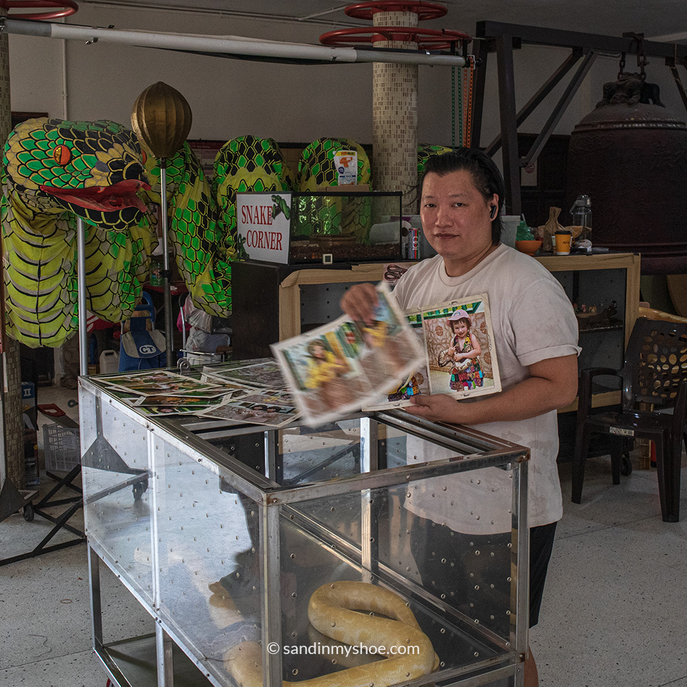 Man at the Snake Temple in Penang offering souvenir photos of tourists posing with a python.