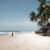 Surfer walking along the beach in Arugam Bay with a surfboard during August, showing the sunny east‑coast conditions travellers consider when asking if August is a good month to visit Sri Lanka.