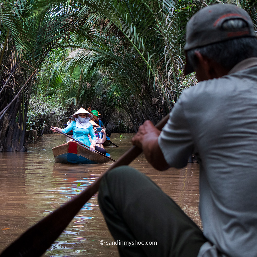 A woman rowing a small boat with tourists along a calm river.