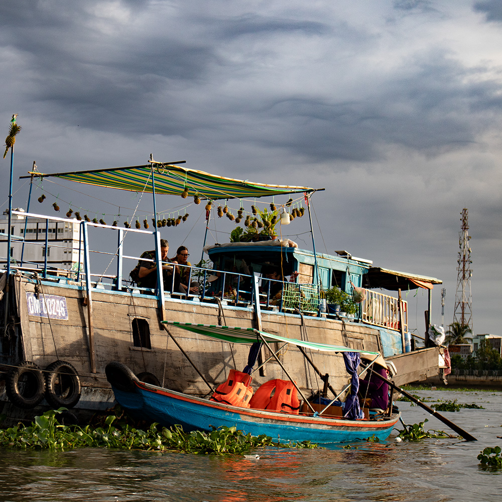 Tourists eating breakfast on a larger wooden boat at dawn at Cai Rang floating market in Can Tho, Mekong Delta, Vietnam