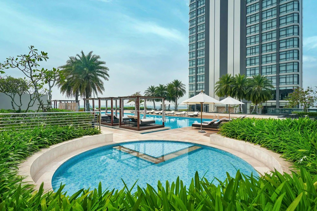 Outdoor pool at Sheraton Can Tho with surrounding greenery, sun loungers, and views of the hotel building.