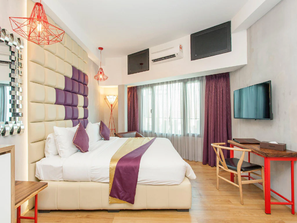 Spacious room at Le Dream Boutique Hotel with a large bed, desk, chair, and TV.