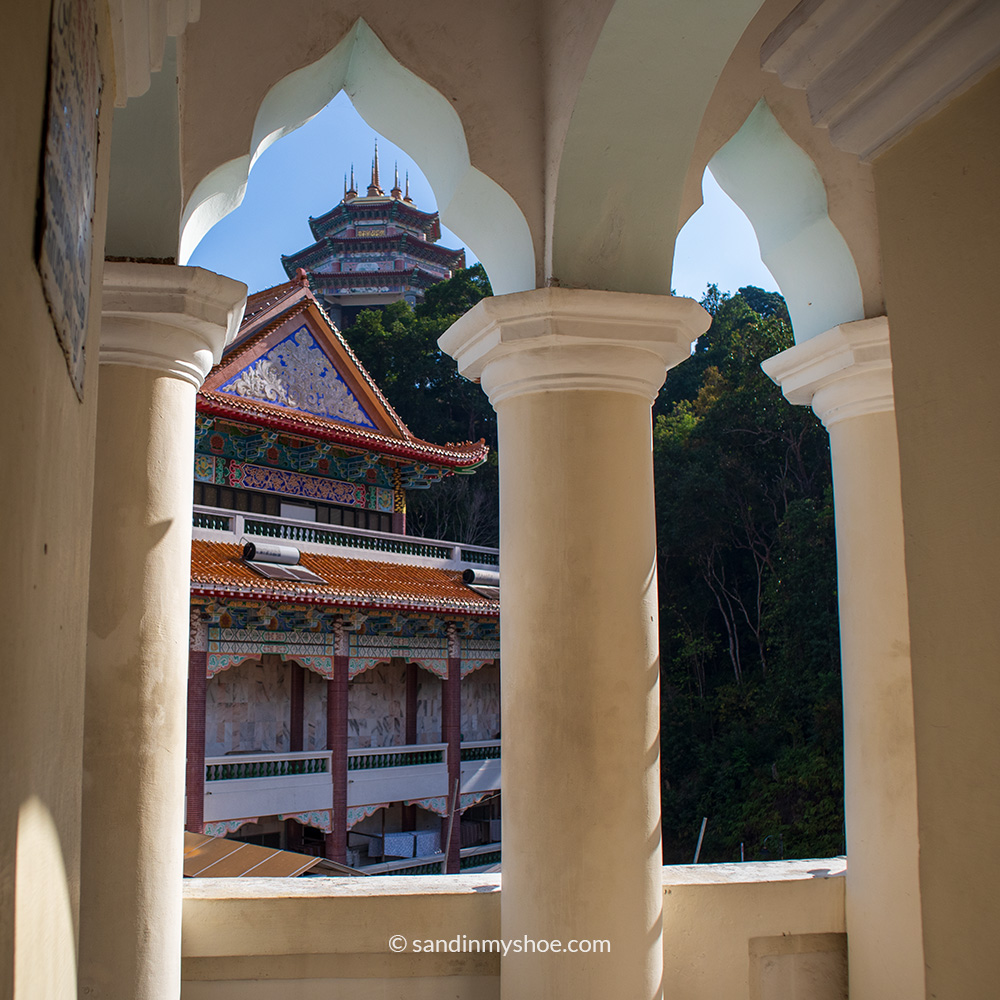 Decorative pillars in the foreground with multiple Kek Lok Si temple structures rising behind them on the hillside.