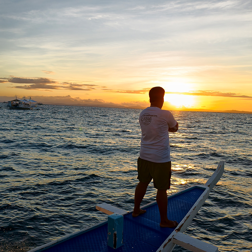 dive master standing at the edge of the boat while the sun is rising.