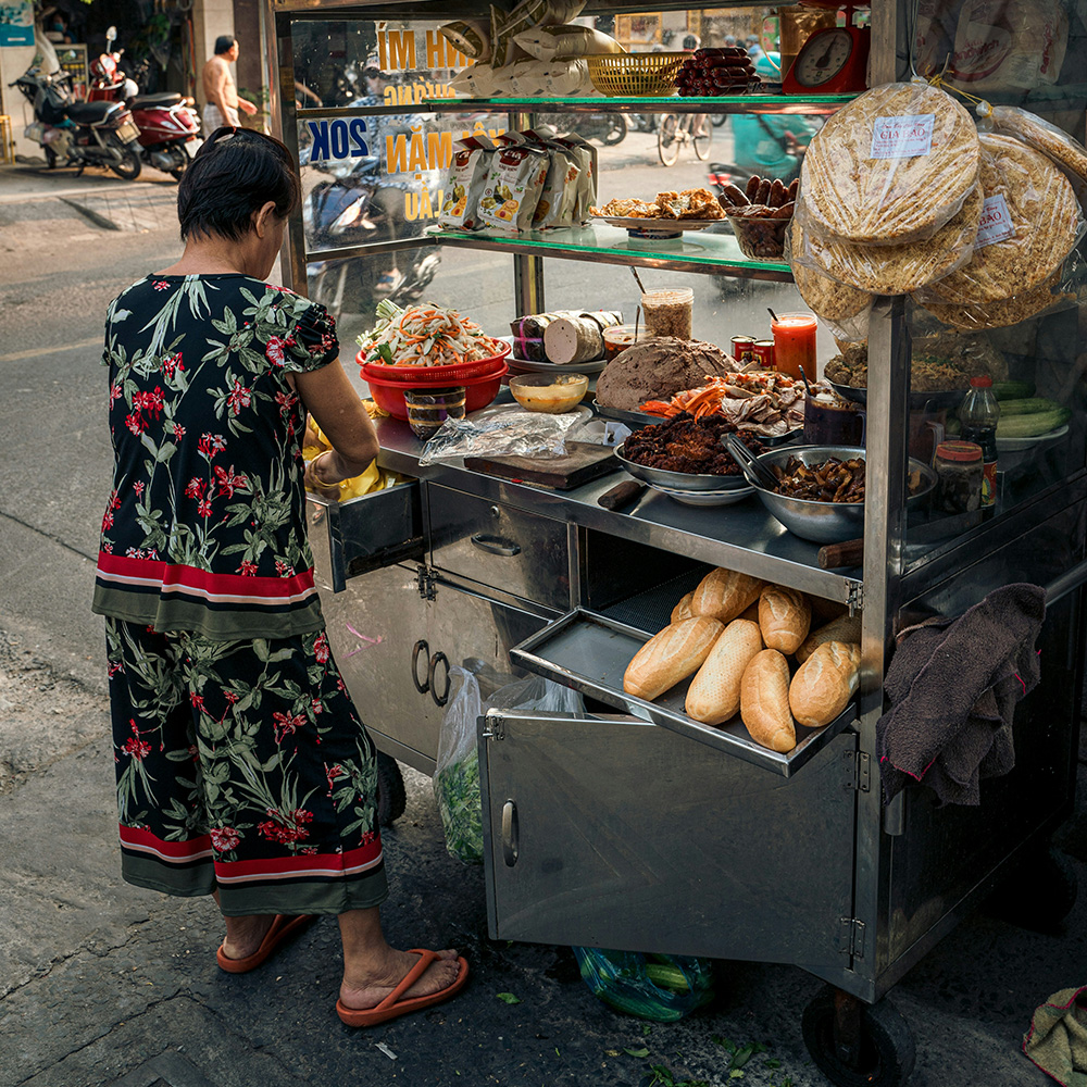 Woman preparing a bánh mì at a street stall in Vietnam.